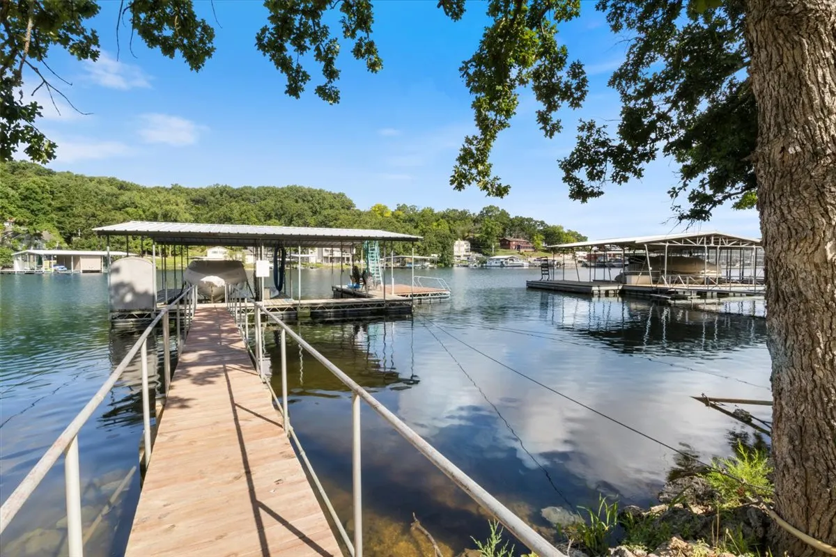 This image features a private dock extending over tranquil water, surrounded by lush trees and boathouses in the distance. The dock is well-suited for boating and fishing, and the calm ambiance invites relaxation or an afternoon picnic by the lake.