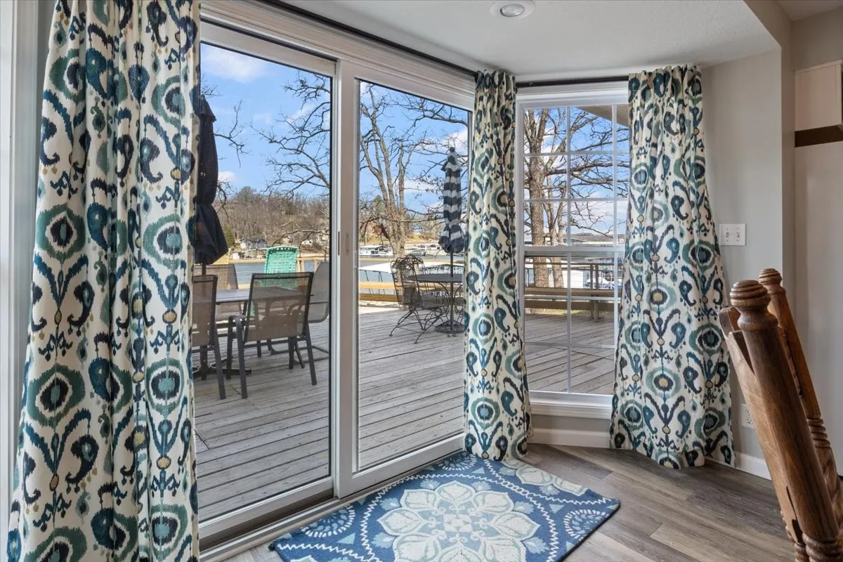 A tranquil room with large glass doors, decorative curtains, and an area rug. The view through the doors suggests immediate access to an outdoor deck or lake, blending indoor comfort with outdoor scenery.