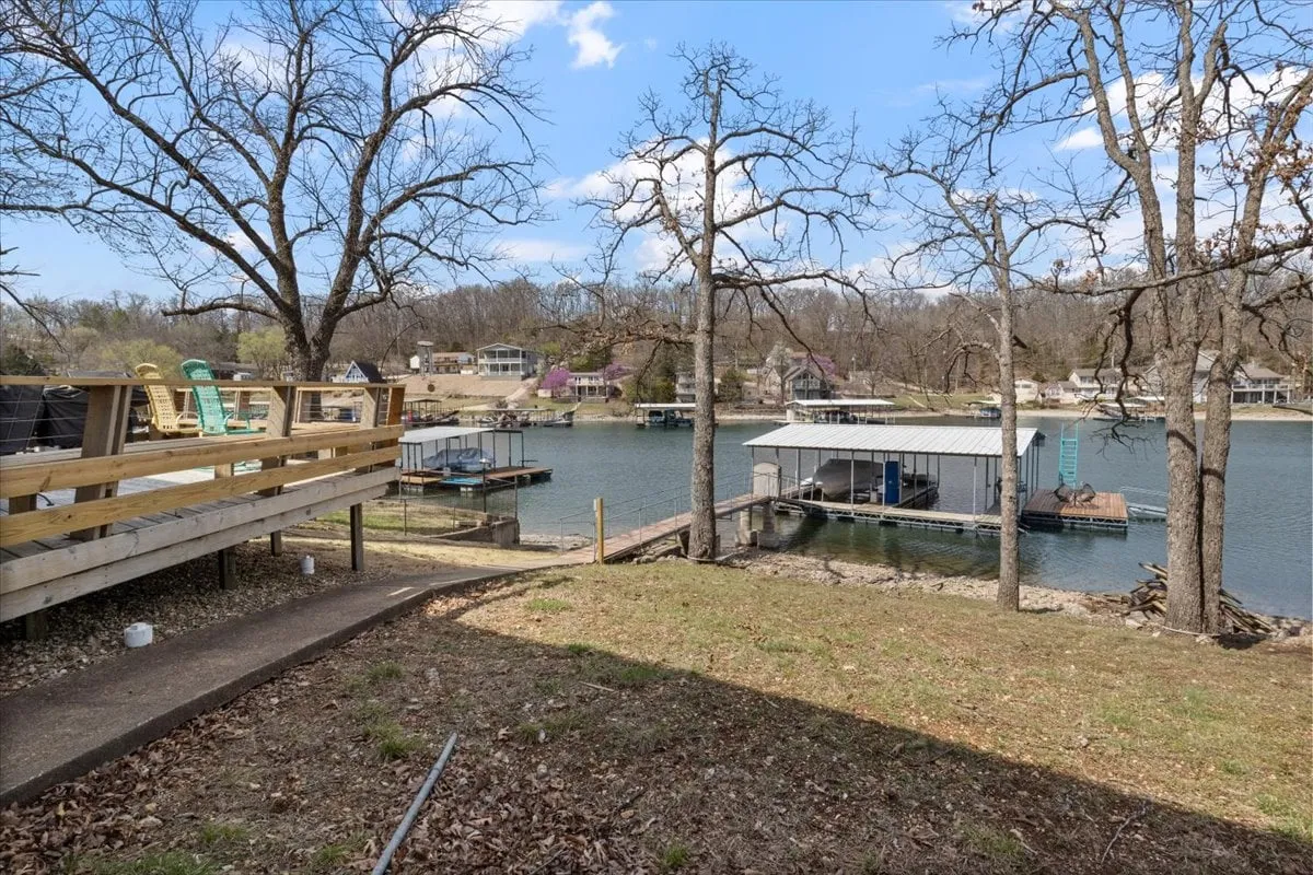 A peaceful scene looking out over the lake, with a broad deck and distant docks framed by tall trees. The space is ideal for relaxing after a day on the water, enjoying sunset views, and gathering for barbecues or morning coffee with family and friends.