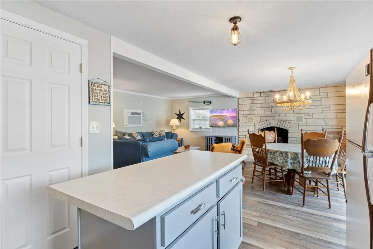 This image captures a spacious, open-plan interior featuring the kitchen island, a dining table with chairs, a cozy sofa in the living area, a fireplace, and a chandelier. The room is warmly lit and styled for relaxation and social interaction, making it perfect for family meals, conversations, and movie nights.