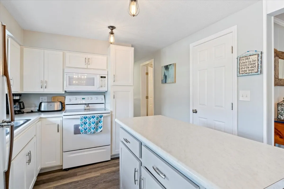 The kitchen features a spacious island, white cabinetry, modern stainless steel appliances, and stylish pendant lighting. The setup is perfect for family gatherings, meal prep, or entertaining.