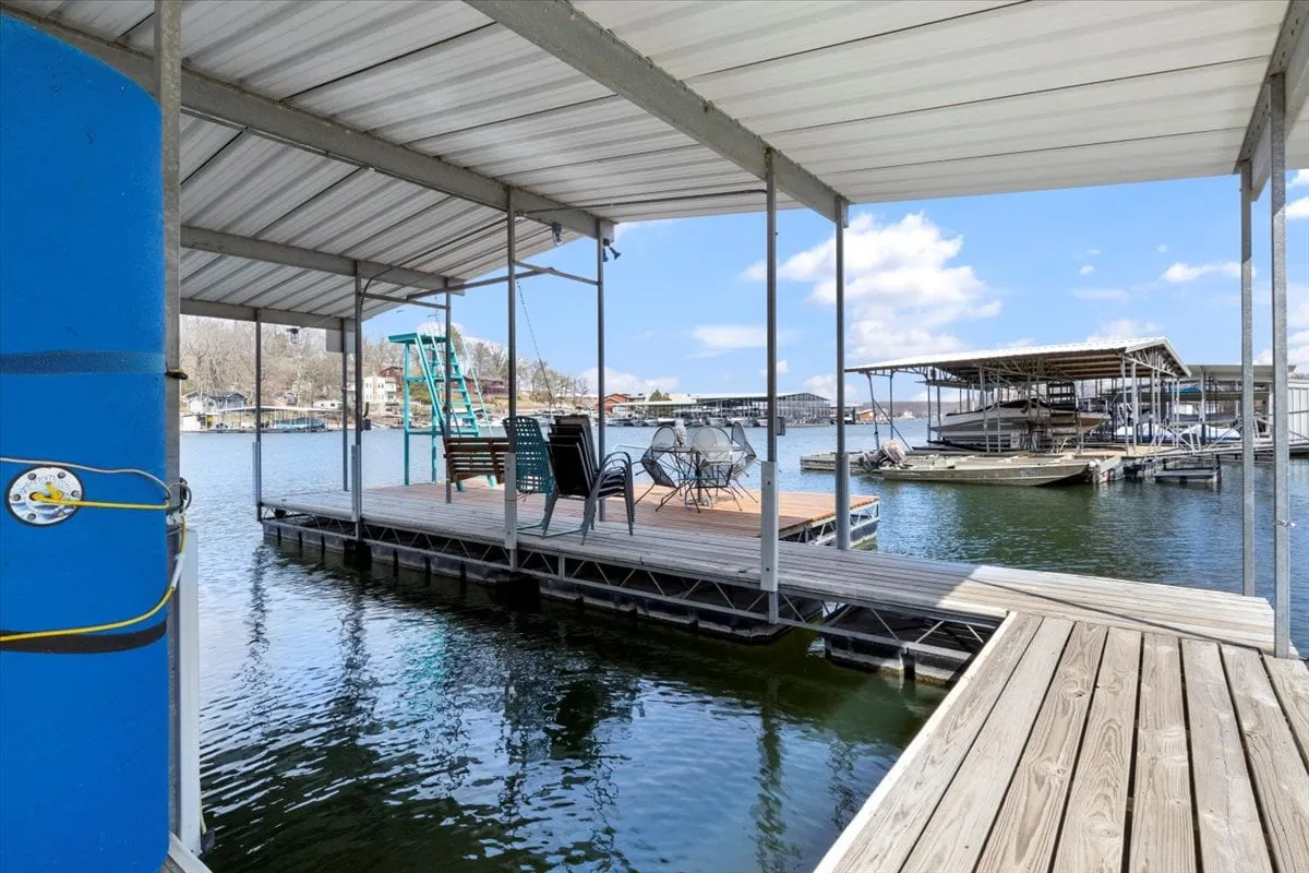 A lakeside dock with comfortable chairs and a table overlooking the water, surrounded by serene natural landscape. The setting suggests opportunities for fishing, boating, relaxing with a drink, or enjoying peaceful sunrises and sunsets.