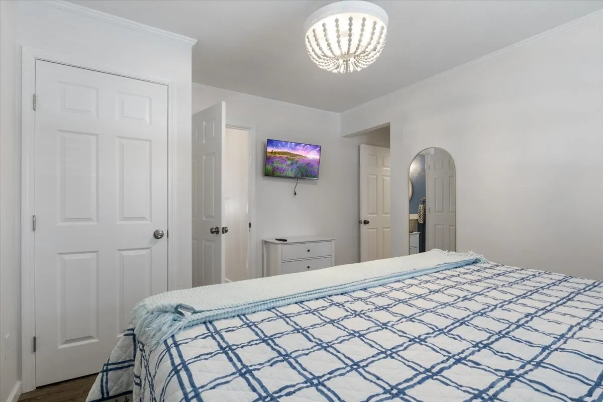 A cozy bedroom with a textured blanket on the bed, elegant chandelier, television, and crisp white doors. The modern and comfortable setup invites relaxation and privacy.