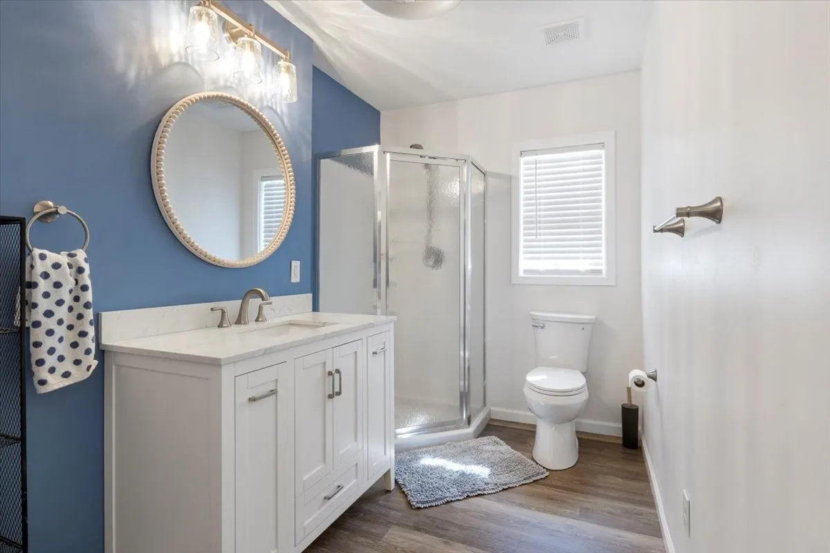 A stylish bathroom featuring a round mirror, modern shower enclosure, vanity with ample space, and a toilet. The room is bathed in morning light, evoking a sense of freshness and relaxation after a day outdoors.