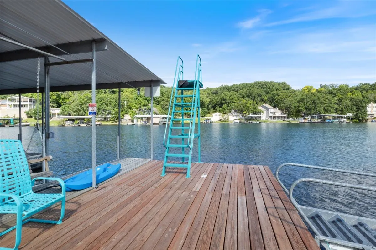 A joyful summer setting with a wooden dock, a bright blue kayak, a dive ladder for easy water access, and expansive lake views. The scene radiates fun and leisure, inviting thoughts of swimming, kayaking, fishing, and gathering for water-based play.
